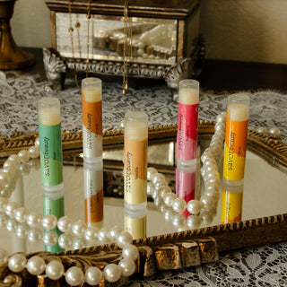 Set of 5 lip balm tubes on a decorative mirror with a vintage jewelry box in the background.