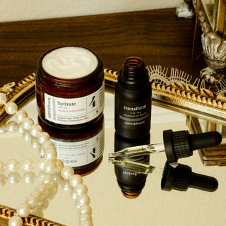 Skincare products including a jar and bottles on a reflective surface with decorative elements.