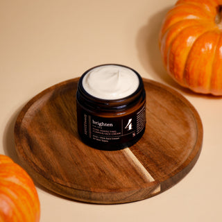 Jar of cream labeled 'brighten' on a wooden tray with pumpkins in the background