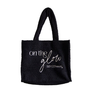 Black fleece tote bag with 'on the glow' text and 'savor beauty' logo on a white background