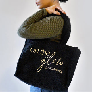 Person holding a black fleece tote bag with 'on the glow' text, wearing a green sweater.