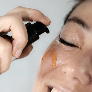 A close up shot of a Korean woman applying the Raspberry Seed Serum to her cheek. The texture is golden and she looks glowing and happy