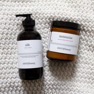 Body Serum and body cream bottles laying on a white chunky knit blanket
