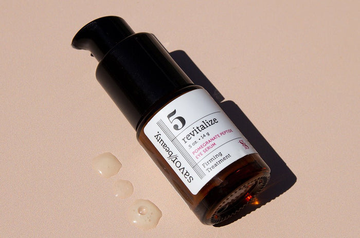 Close up shot of Pomegranate Eye Serum bottle and 3 drops of the product on a beige backround 