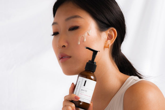 Young woman with clear skin and pearl cleansing cream on face posing with cleanser bottle 