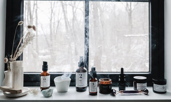 Skincare products sitting on a windowsill with inscence and snow outside the window