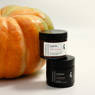 Savor Beauty's AM + PM Pumpkin duo stacked in front of a large orange pumpkin on a clean white background. The top jar is Truffle Face Cream labeled 'hydrate' and the bottom jar is Sleeping Beauty Pumpkin Cream labeled 'enchant'.