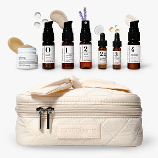 Savor Beauty's glass skin discovery kit skincare arranged on a white background, featuring five amber dropper bottles labeled 0 to 4, with texture shots, and a quilted cream zip case with a bow. The case has a visible SAVOIBEAUTY logo patch.