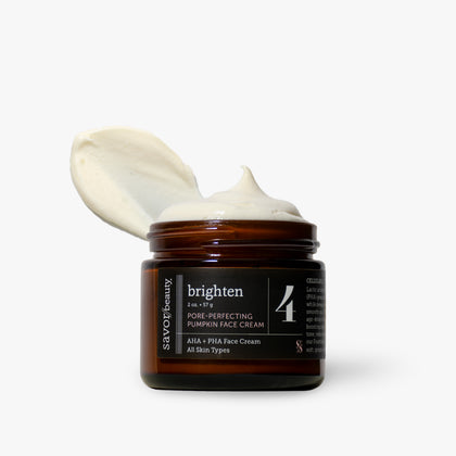 An open amber glass jar of Savor Beauty Brighten Pone Perfecting Pumpkin Face Cream with a dollop of white cream on top, set against a clean off-white background.