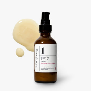 Savor Beauty Purify Rosemary Cloud Cleanser in an amber glass bottle with a black pump dispenser, shown against a light gray background with a cream-colored liquid splash behind it.