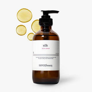 Savor Beauty Silk Body Serum in an amber glass pump bottle with a black dispenser and white label, shown on a light gray background with four translucent yellow circular ingredient slices floating behind it.