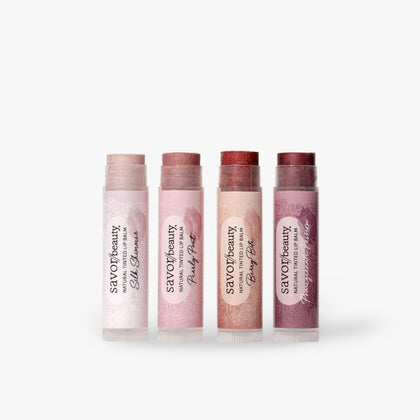 Four lip balm tubes from savor beauty lined up on a light gray background. The tubes are in shades of pale pink, dusty rose, peach, and mauve, with white labels featuring black text.