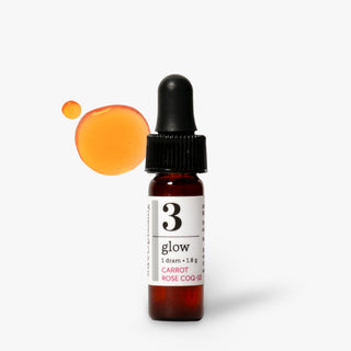 A small amber glass dropper bottle labeled '3 glow' with a black dropper cap, shown on a light gray background with an orange liquid droplet graphic behind it.