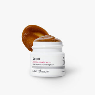 A white jar of Savor Beauty Detox Manuka Honey Mask with a dollop of the thick, glossy brown mask applied to the lid, set against a clean white background.