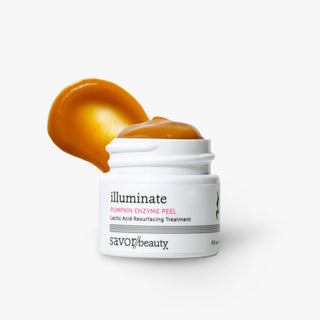 A white jar of Savor Beauty illuminate Pumpkin Enzyme Peel with a dollop of orange pumpkin-colored product on top and a matching orange smear behind it, set against a clean white background.