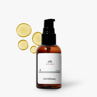 Savor Beauty Silk Body Serum in an amber glass bottle with a black pump dispenser and a white label, shown on a light gray background with four yellow circular droplet graphics on the left.