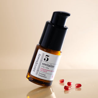 savor beauty revitalize pomegranate peptide eye serum on a clean cream backround angled on a reflective surface with pomegranate seeds 