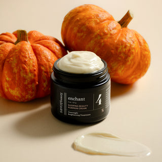 Savor Beauty's black label  SLEEPING BEAUTY PUMPKIN CREAM with white cream visible at the top, styled with two orange pumpkins and a smear of the cream on a warm beige background.