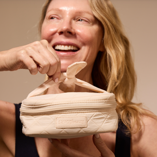 Woman smiling holding a quilted makeup bag.