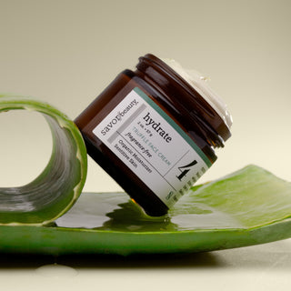 Skincare jar labeled 'hydrate' on a green leaf with a beige background