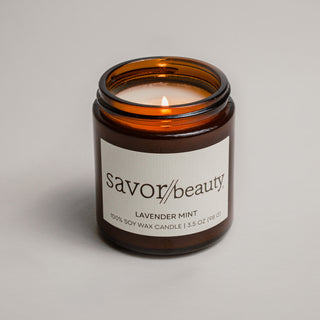 Savor Beauty candle with a lit wick on a neutral background