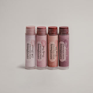 4 tinted lip balm sticks standing next to each other against a grey background