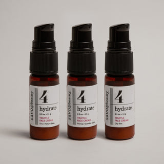 Three travel size bottles of truffle face cream on a gray background