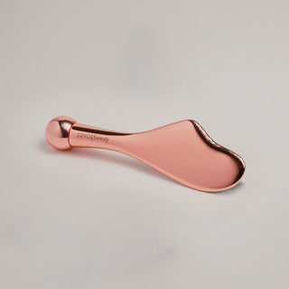 Rose gold gua sha on a light gray background