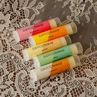 Five Savor Beauty lip balm tubes on a lace background