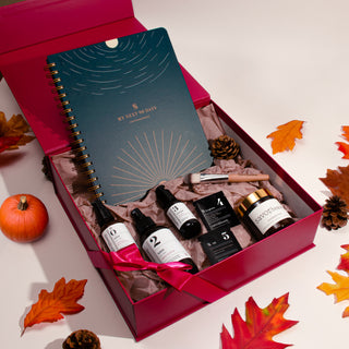 Gift box with skincare products and a notebook on a decorative background with autumn leaves.