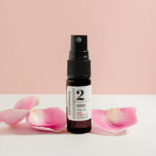 Skincare bottle with a label on a pink and white background with rose petals