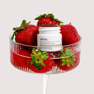 White jar of strawberry peel in a cup surrounded by fresh strawberries