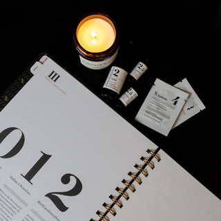 Open Savor Planner with a lit candle and travel size skincare bottles on a dark background