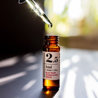 close up shot of 1 dram glass bottle of savor beauty heal blue tansy 2% bakuchiol serum on a sunny blurred backround