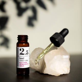 close up shot of 1 dram glass bottle of savor beauty heal blue tansy 2% bakuchiol serum on a crystal in a neutral light green backround