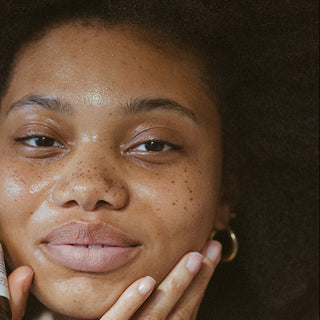 Woman holding a skincare bottle near her face against a neutral background