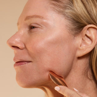 Woman guasha-ing her face with a beige background