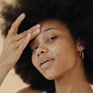 Woman wearing a white tank top and gold jewelry applying face cleanser