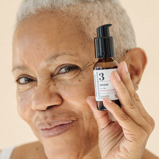 Woman holding a skincare product bottle against her face on a beige background