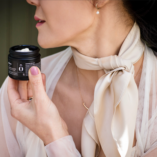 Woman holding neck cream jar, wearing a beige silk scarf.