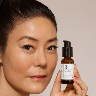 Woman holding a skincare serum bottle with a neutral background
