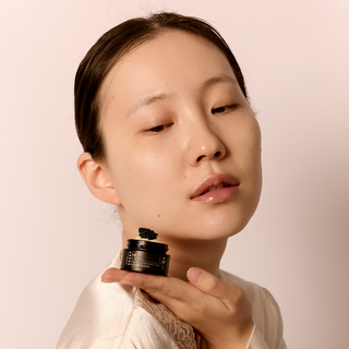 Woman holding a skincare product against a plain background