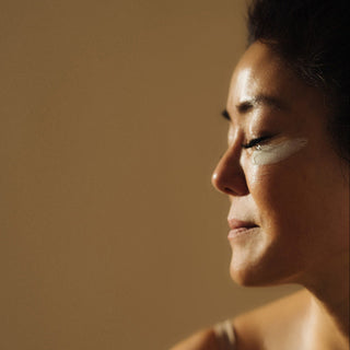 woman with face cream on her cheek smiling, eyes closed, neutral background