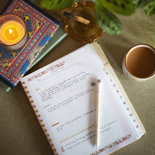 Open planner with writing on a table with a candle and mug of tea.