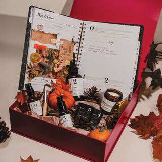 Open planner with decorative items including bottles and pumpkins, surrounded by autumn leaves.