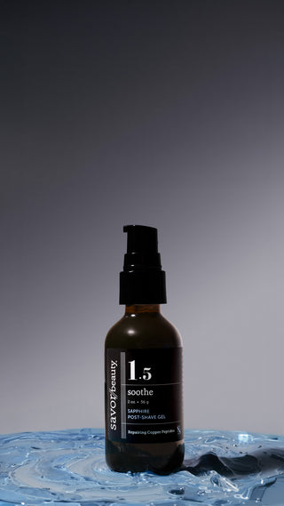 Dark amber and black label bottle of Savor Beauty's Sapphire Post-Shave Gel standing on a large texture shot of the sapphire blue texture on a blue/gray background