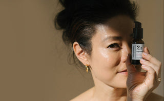 Founder Angela Jia Kim holding blue tansy serum bottle near her face against a neutral background